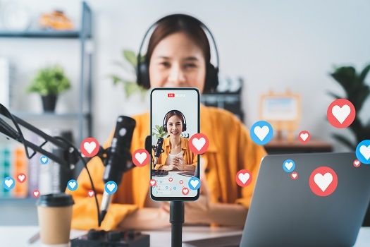 A content creator recording a live video on her smartphone with engagement icons floating around — showing how to make your brand stand out on social media through authentic content.